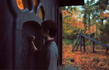 Movie still from “Gretel & Hansel” (2020), directed by Oz Perkins – A person is painting on the wall of a building; Medium shot, Over the shoulder angle