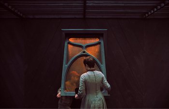 Movie still from “Gretel & Hansel” (2020), directed by Oz Perkins – A woman in a dress looking into a window; Medium shot, Over the shoulder angle