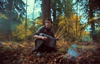 Movie still from “Gretel & Hansel” (2020), directed by Oz Perkins – A man sitting on the ground holding a guitar; Medium shot, Low angle