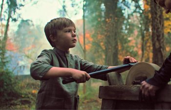 Movie still from “Gretel & Hansel” (2020), directed by Oz Perkins – A young boy using an electric saw to cut wood; Medium shot, Low angle