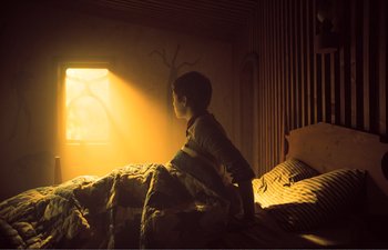 Movie still from “Gretel & Hansel” (2020), directed by Oz Perkins – A child sitting on a bed looking out a window; Wide shot, Low angle
