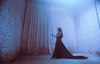 Movie still from “Gretel & Hansel” (2020), directed by Oz Perkins – A woman in a long black dress standing next to a curtain; Wide shot, Low angle