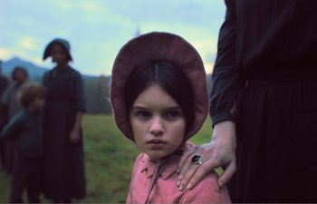 Movie still from “Gretel & Hansel” (2020), directed by Oz Perkins – A young girl wearing a pink dress and a pink hat; Close Up shot, Over the shoulder angle