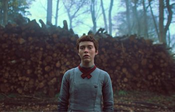 Movie still from “Gretel & Hansel” (2020), directed by Oz Perkins – A young man standing in front of a pile of wood; Medium shot, Low angle