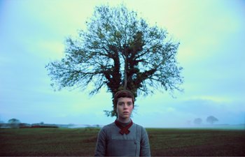 Movie still from “Gretel & Hansel” (2020), directed by Oz Perkins – A young man standing in front of a large tree; Medium shot, Low angle