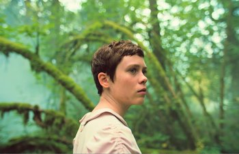 Movie still from “Gretel & Hansel” (2020), directed by Oz Perkins – A woman with short brown hair stands in front of trees; Close Up shot, Low angle