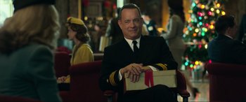 Movie still from “Greyhound” (2020), directed by Aaron Schneider – A man in a suit and tie holding a gift box; Medium shot, Over the shoulder angle