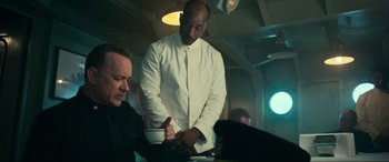 Movie still from “Greyhound” (2020), directed by Aaron Schneider – A man standing at a table with a bowl of food; Medium shot, Over the shoulder angle