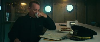 Movie still from “Greyhound” (2020), directed by Aaron Schneider – A man sitting at a table drinking a cup of coffee; Medium shot, High angle
