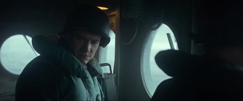 Movie still from “Greyhound” (2020), directed by Aaron Schneider – A man wearing a hat and a jacket looking out of a window; Close Up shot, Low angle