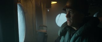 Movie still from “Greyhound” (2020), directed by Aaron Schneider – A man wearing a hat and a jacket looking out of a window; Close Up shot, Low angle