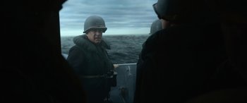Movie still from “Greyhound” (2020), directed by Aaron Schneider – A man in a helmet is standing on a boat in the ocean; Medium shot, Over the shoulder angle