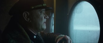 Movie still from “Greyhound” (2020), directed by Aaron Schneider – A man wearing a hat looking out a window; Close Up shot, Low angle