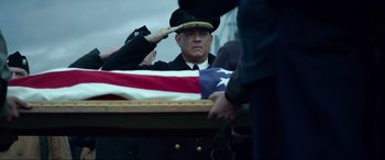 Movie still from “Greyhound” (2020), directed by Aaron Schneider – An officer saluting a flag at a military ceremony; Medium shot, Low angle