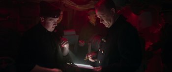 Movie still from “Greyhound” (2020), directed by Aaron Schneider – Two men are looking at papers in a dimly - lit room; Medium shot, Low angle