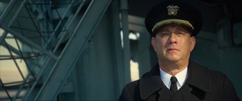 Movie still from “Greyhound” (2020), directed by Aaron Schneider – A man in a uniform is standing in front of a building; Close Up shot, Low angle