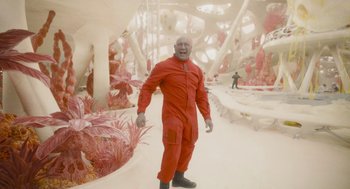 Movie still from “Guardians of the Galaxy Vol. 3” (2023), directed by James Gunn – A man in a red suit standing next to some pink plants; Wide shot, High angle