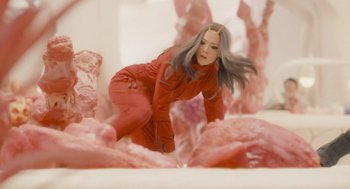 Movie still from “Guardians of the Galaxy Vol. 3” (2023), directed by James Gunn – A woman in a red suit standing in a room filled with pink rocks; Medium shot, High angle