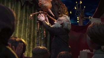 Movie still from “Guillermo del Toro's Pinocchio” (2022), directed by Guillermo del Toro – An old man holding a puppet in front of a group of people; Medium shot, Low angle