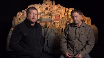 Movie still from “Guillermo del Toro's Pinocchio” (2022), directed by Guillermo del Toro – A couple of men sitting next to each other in front of a building; Medium shot, High angle