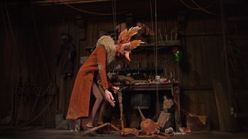 Movie still from “Guillermo del Toro's Pinocchio” (2022), directed by Guillermo del Toro – A person in a costume standing next to a bunch of puppets; Wide shot, Low angle