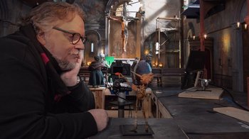 Movie still from “Guillermo del Toro's Pinocchio” (2022), directed by Guillermo del Toro – A man sitting in front of a statue in a room; Medium shot, Over the shoulder angle