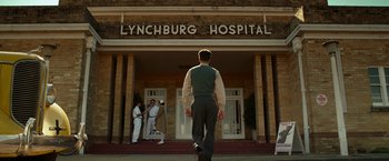 Movie still from “Hacksaw Ridge” (2016), directed by Mel Gibson – A man walking in front of a building with people standing around; Wide shot, Low angle