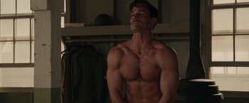 Movie still from “Hacksaw Ridge” (2016), directed by Mel Gibson – A man with no shirt is standing in a room; Medium shot, Low angle