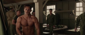 Movie still from “Hacksaw Ridge” (2016), directed by Mel Gibson – A shirtless man standing next to a man in a uniform; Medium shot, Over the shoulder angle