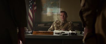 Movie still from “Hacksaw Ridge” (2016), directed by Mel Gibson – A man sitting at a desk in front of an american flag; Medium shot, Low angle