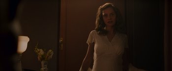 Movie still from “Hacksaw Ridge” (2016), directed by Mel Gibson – A woman in a white dress standing next to a door; Medium shot, Over the shoulder angle