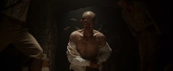 Movie still from “Hacksaw Ridge” (2016), directed by Mel Gibson – A man with a shaved head is standing in a dark room; Medium shot, Low angle