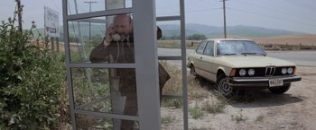 Movie still from “Halloween” (1978), directed by John Carpenter – A man talking on a phone next to a car; Wide shot, High angle