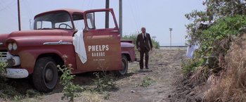Movie still from “Halloween” (1978), directed by John Carpenter – A man walking next to an old red truck; Wide shot, Low angle