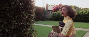 Movie still from “Halloween” (1978), directed by John Carpenter – A woman is holding a book while standing next to a tree; Medium shot, Low angle