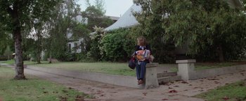 Movie still from “Halloween” (1978), directed by John Carpenter – A woman sitting on a concrete bench holding a baby; Wide shot, High angle