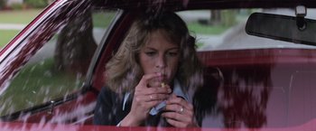 Movie still from “Halloween” (1978), directed by John Carpenter – A woman sitting in the back seat of a car eating a hot dog; Close Up shot, Low angle