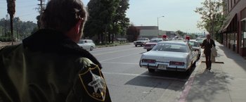 Movie still from “Halloween” (1978), directed by John Carpenter – A man standing on the side of a road next to cars; Wide shot, Over the shoulder angle