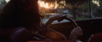 Movie still from “Halloween” (1978), directed by John Carpenter – A person driving a car at night with the sun setting behind them; Close Up shot, Over the shoulder angle