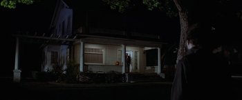 Movie still from “Halloween” (1978), directed by John Carpenter – A man standing on the porch of a house at night; Wide shot, Low angle