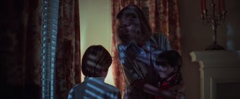 Movie still from “Halloween” (1978), directed by John Carpenter – A woman and two children are standing in a living room; Medium shot, Over the shoulder angle