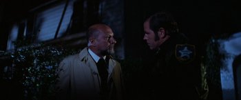 Movie still from “Halloween” (1978), directed by John Carpenter – Two men are standing in the dark looking at each other; Medium shot, Over the shoulder angle