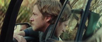 Movie still from “Halloween” (2018), directed by David Gordon Green – A man with long blonde hair is looking out the car window; Close Up shot, Over the shoulder angle