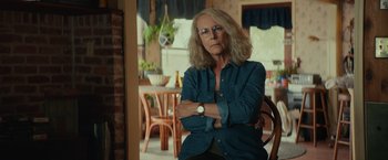 Movie still from “Halloween” (2018), directed by David Gordon Green – An older woman sitting in a chair with her arms crossed; Medium shot, Over the shoulder angle