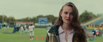 Movie still from “Halloween” (2018), directed by David Gordon Green – A woman standing in a field with a football field in the background; Close Up shot, Over the shoulder angle