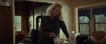 Movie still from “Halloween” (2018), directed by David Gordon Green – A woman in a green jacket is making a smoothie; Medium shot, Over the shoulder angle