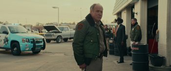 Movie still from “Halloween” (2018), directed by David Gordon Green – A man in a green jacket standing in front of a crowd of onlookers; Medium shot, Over the shoulder angle