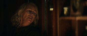 Movie still from “Halloween” (2018), directed by David Gordon Green – An older woman wearing glasses looking out of a window; Close Up shot, Over the shoulder angle