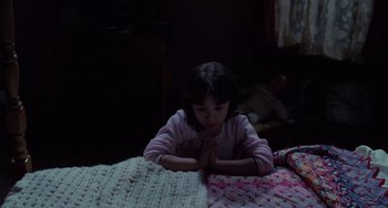 Movie still from “Halloween 4: The Return of Michael Myers” (1988), directed by Dwight H. Little – A little girl sitting on top of a bed with her hands folded; Medium shot, High angle