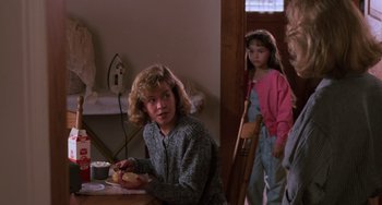 Movie still from “Halloween 4: The Return of Michael Myers” (1988), directed by Dwight H. Little – A woman sitting at a table holding a piece of fruit; Medium shot, Over the shoulder angle